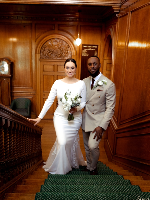 A Bride And Groom Posing Together On A Classic Green Carpeted Wooden Staircase In A Formal Venue.